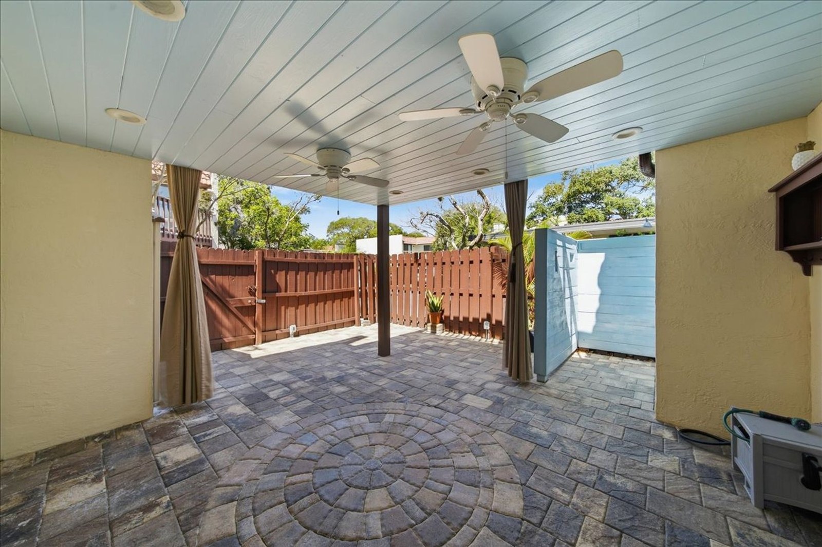 Covered private patio with ceiling fan, pavers, and wood privacy fence