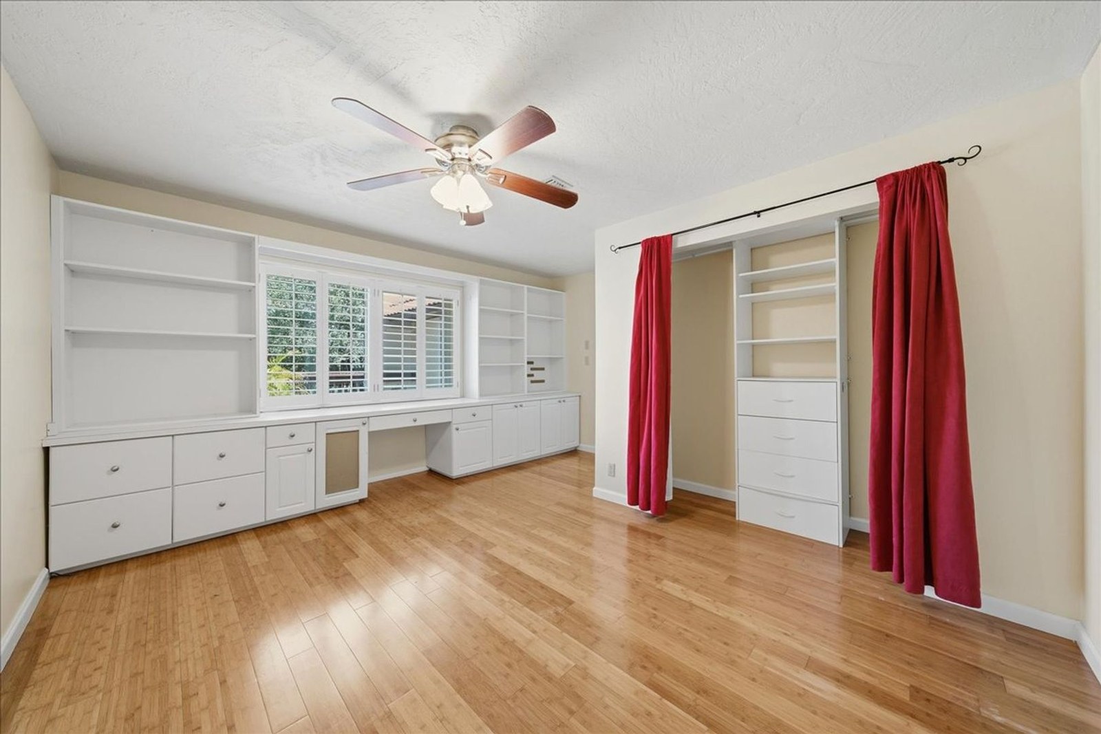 Second bedroom with built-in dresser, plantation shutters, and ceiling fan