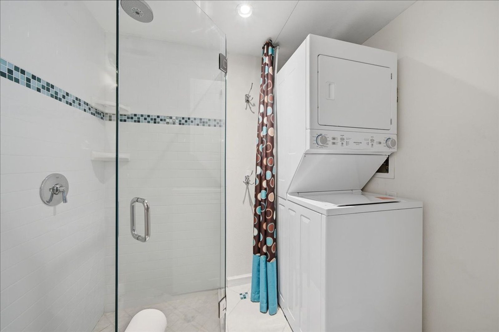 Glass-enclosed shower and full-size stacked washer and dryer