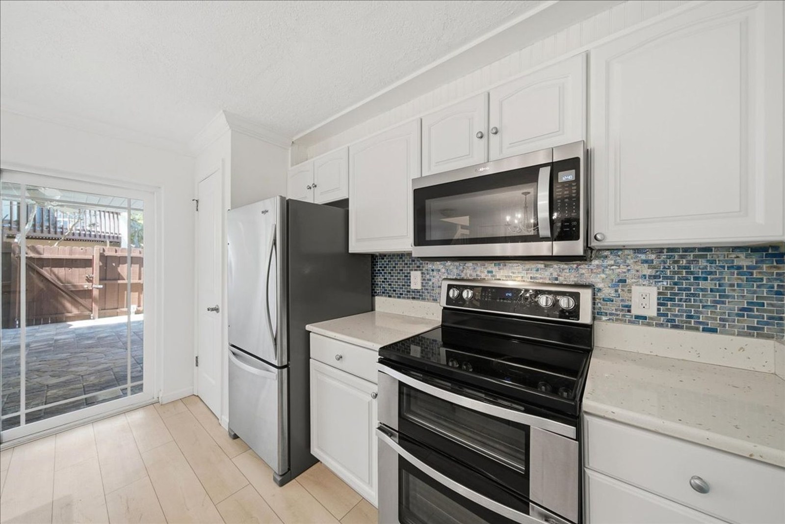 Kitchen with stainless range and microwave, coastal glass-tile backsplash, and solid wood cabinetry at 8760 Live Oak Ct
