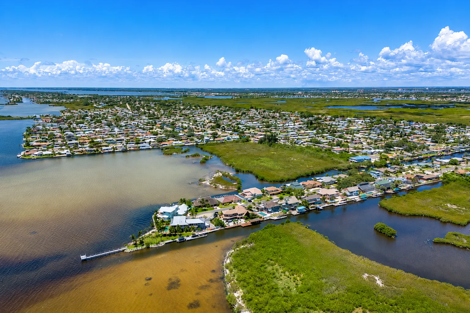 Aerial view of the North Banana River Drive waterfront neighborhoods on Merritt Island, with canals, boat docks, and the Banana River stretching toward the Cape Canaveral launch pads